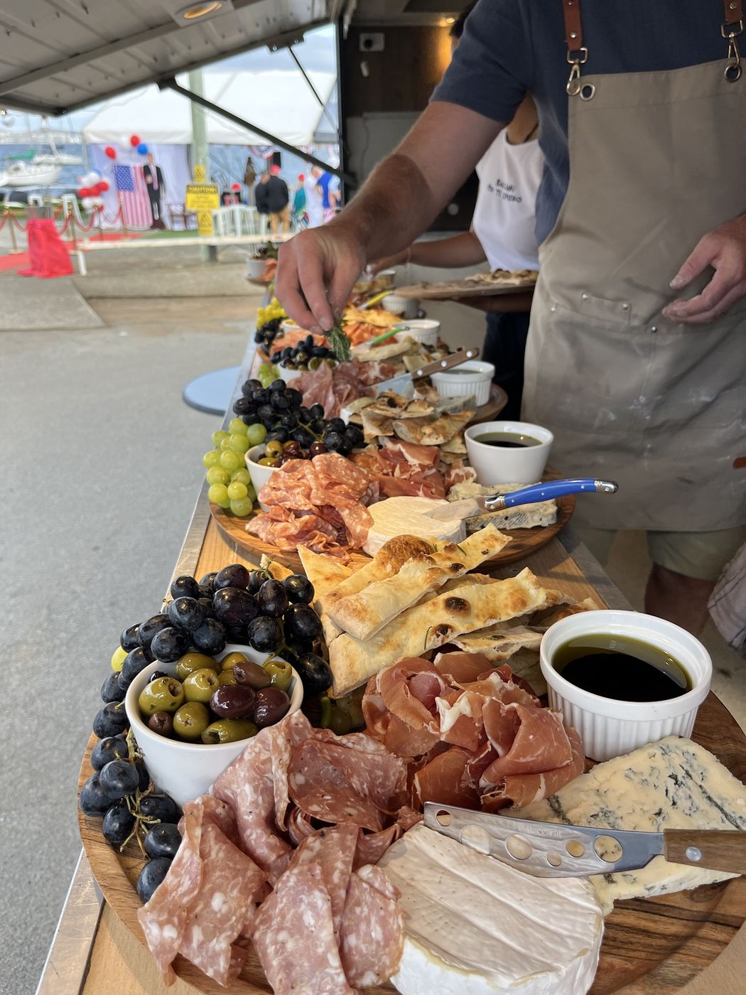 A grazing board of cured meats, cheeses, olives and fruit being laid out at an event