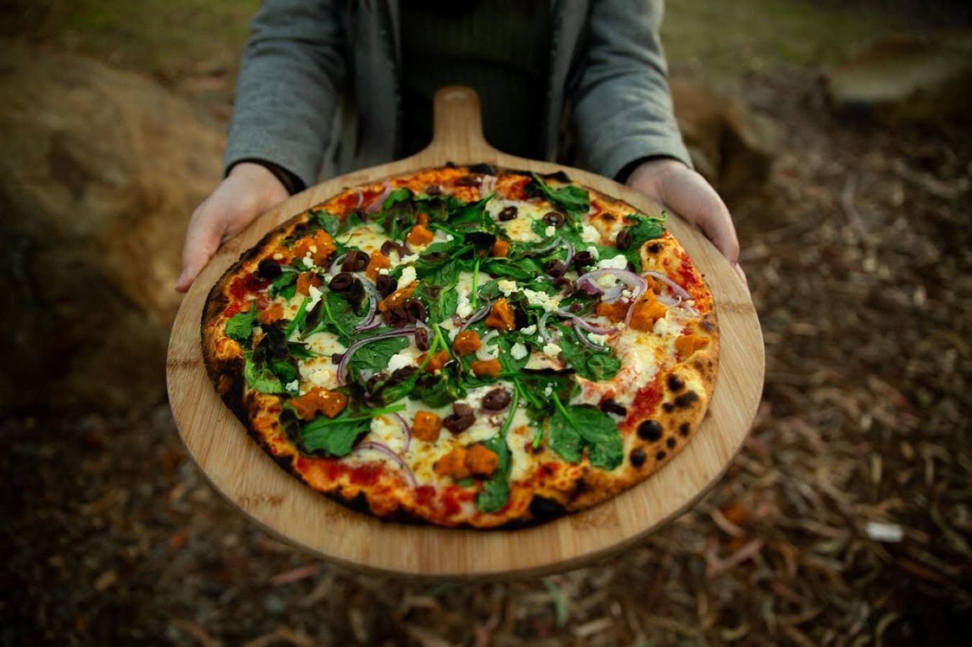 A wood-fired pizza on a wooden paddle
