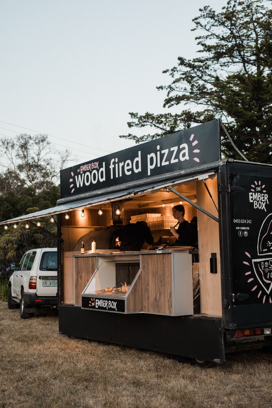 The Ember Box wood fired pizza trailer set up at an event at dusk